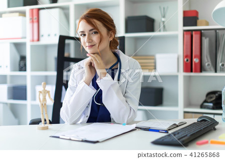 A beautiful young girl in a white robe is sitting at a table in the office. 41265868