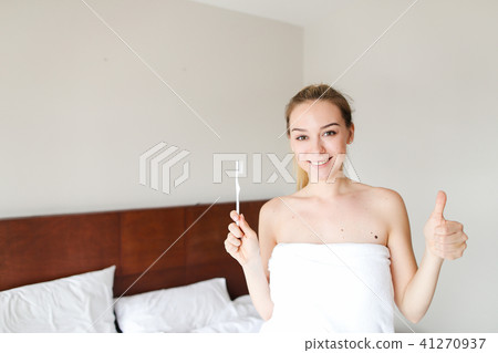 Young nice woman wrapped in white towel standing with toothbrush near bed, showing thumbs up. 41270937