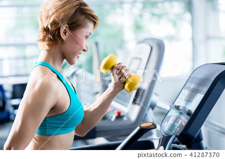 Asian woman walking on treadmill holding dumbbell Asian woman walking on treadmill holding dumbbell 41287370