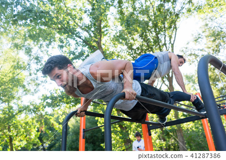 Strong young man supporting his friend while doing pull-ups Strong young man supporting his friend while doing pull-ups 41287386