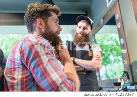 Bearded young man thinking of a trendy change of look in the hair salon Bearded young man thinking of a trendy change of look in the hair salon 41287387