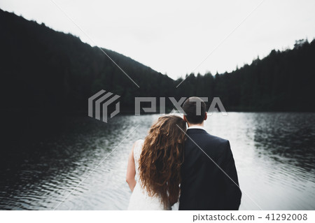 Young newly wed couple, bride and groom kissing, hugging on perfect view of mountains, blue sky 41292008