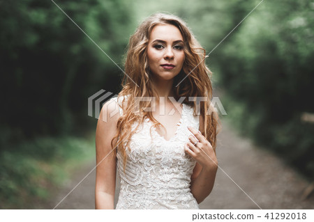 Beautiful bride in elegant white dress holding bouquet posing in park Beautiful bride in elegant white dress holding bouquet posing in park 41292018