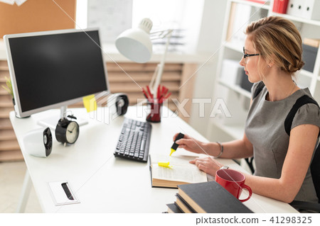 A young girl is sitting at a table in the office, holding a yellow marker in her hand. Before the A young girl is sitting at a table in the office, holding a yellow marker in her hand. Before the 41298325