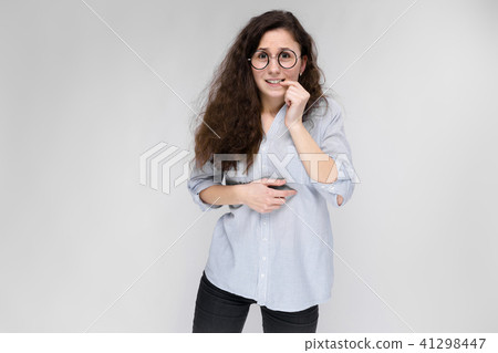 Portrait of a young girl in glasses. Beautiful young girl on a gray background. The girl is gnawing 41298447