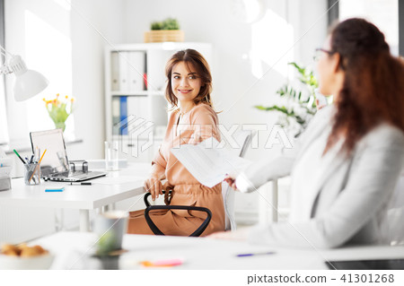 businesswomen giving each other papers at office 41301268