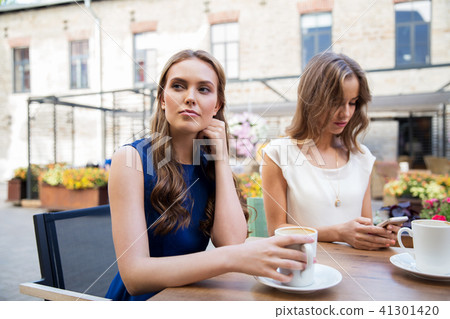 young women with smartphone and coffee at cafe young women with smartphone and coffee at cafe 41301420