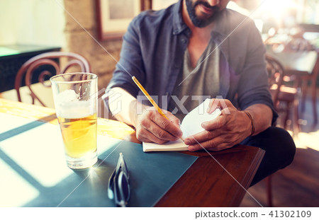 close up of man with beer and notebook at pub 41302109