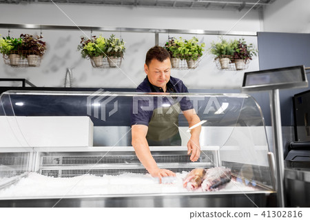 male seller with seafood at fish shop fridge 41302816