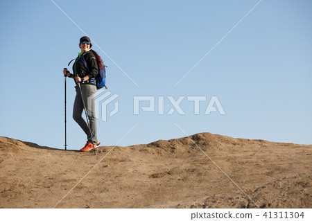 Photo of tourist woman in jacket with backpack and walking sticks 41311304