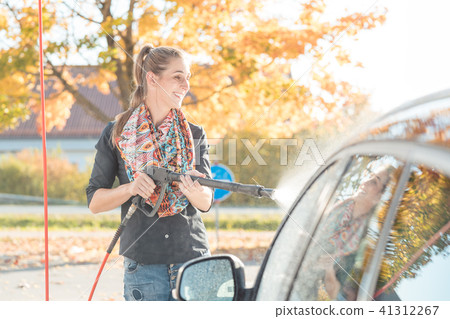 Woman using high pressure nozzle to clean her car Woman using high pressure nozzle to clean her car 41312267