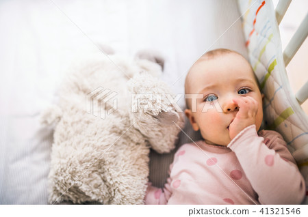 A toddler girl lying in a cot in the bedroom at home, a finger in her mouth. 41321546