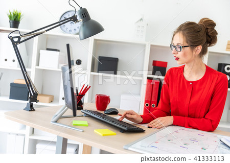 A young girl is sitting at the desk in the office and typing on the keyboard. A magnetic board lies 41333113