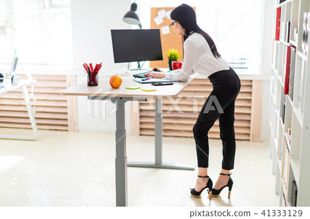 A young girl stands near the table, holds a marker in her hand and prints on the keyboard. A young girl stands near the table, holds a marker in her hand and prints on the keyboard. 41333129