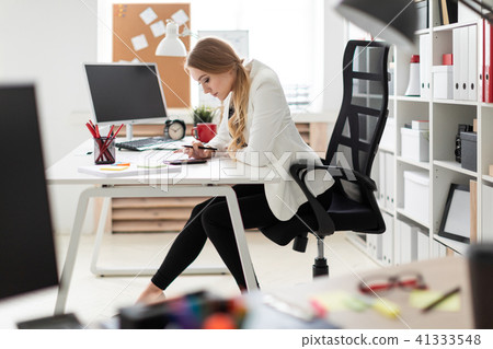 A young girl sits at a computer desk in the office and counts on a calculator on the phone. A young girl sits at a computer desk in the office and counts on a calculator on the phone. 41333548