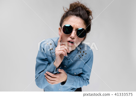 Young brunette girl in round glasses. Hairs are gathered in a bun. The girl put her hand to her chin Young brunette girl in round glasses. Hairs are gathered in a bun. The girl put her hand to her chin 41333575