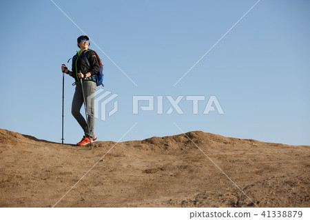 Image of tourist woman in jacket with backpack and walking sticks Image of tourist woman in jacket with backpack and walking sticks 41338879