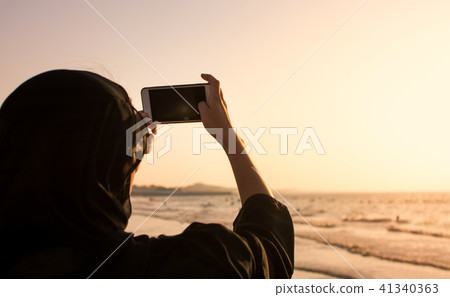 Muslim woman taking a photo on the beach 41340363