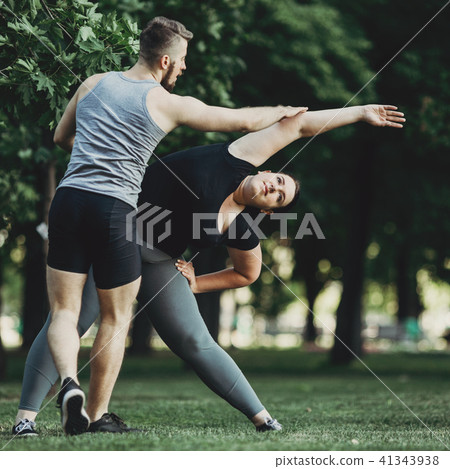 Personal trainer helping overweight woman at street workout 41343938