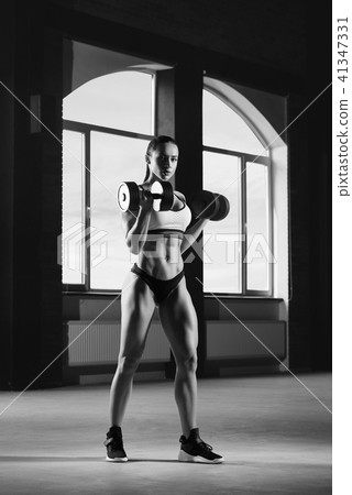 Black and white photo of sexy athletic sporty model lifting heavy dumbbells. Black and white photo of sexy athletic sporty model lifting heavy dumbbells. 41347331