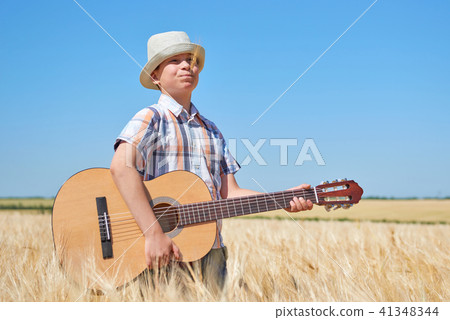 child boy with guitar is in the yellow wheat field 41348344