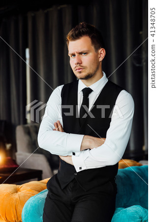 Stylish athletic man in a business costume vest. Sits in the turquoise sofa chair, a serious look. Stylish athletic man in a business costume vest. Sits in the turquoise sofa chair, a serious look. 41348705