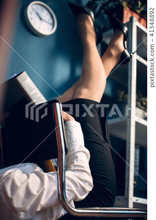 Lady lying on chair in unusual position reading book. 41348892