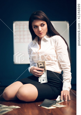 Business woman sitting on table with pile of dollar bills. Business woman sitting on table with pile of dollar bills. 41348899
