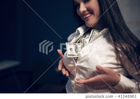 Business woman sitting on table with pile of dollar bills. Business woman sitting on table with pile of dollar bills. 41348901