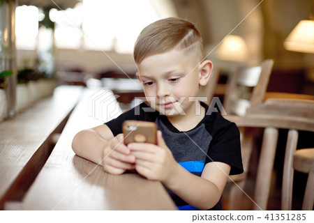 little boy with smartphone sitting at the table little boy with smartphone sitting at the table 41351285