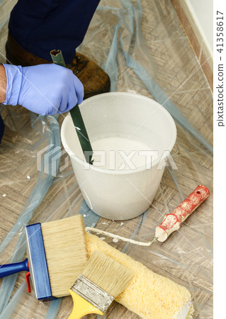 Painter paints the wall with the tint of white. 41358617