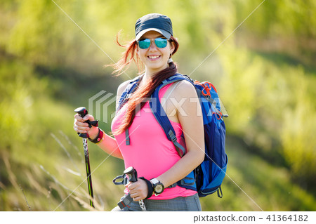Photo of smiling female athlete with walking sticks and backpack with blurred background Photo of smiling female athlete with walking sticks and backpack with blurred background 41364182