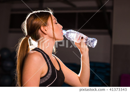 Fitness young woman drinking water in the gym. Muscular woman taking break after exercise 41373343
