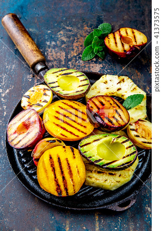 GRILLED FRUITS. Grill fruits - pineapple, peaches, plums, avocado, pear on black cast iron grill pan 41373575