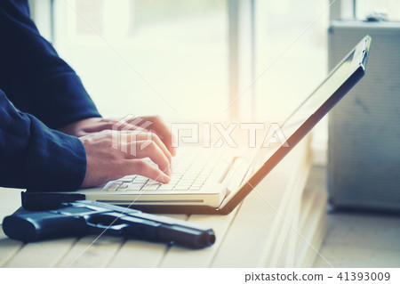 Hacker holding gun working on his computer Hacker holding gun working on his computer 41393009