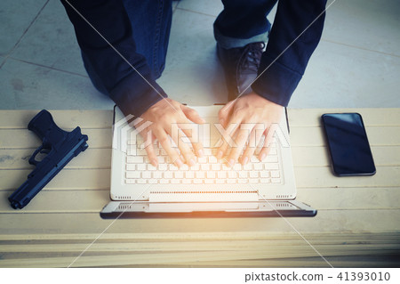 Hacker holding gun working on his computer Hacker holding gun working on his computer 41393010