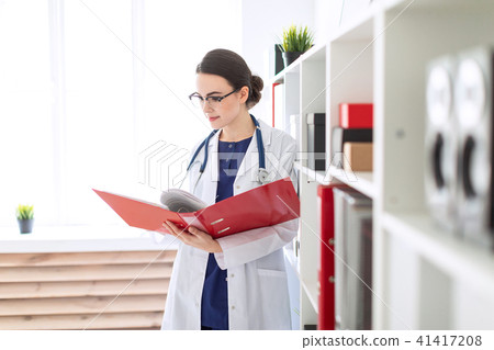A beautiful young girl in a white robe is standing near the shelter and flips through a red folder 41417208