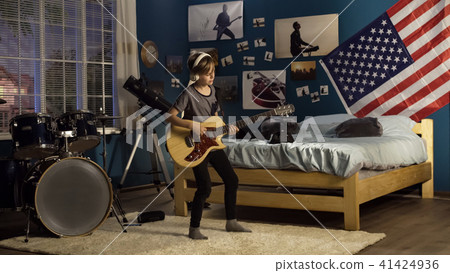 Expressive youngster playing guitar in bedroom 41424936