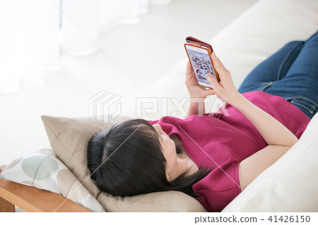 一位年輕的女士躺在沙發上，看著智能手機 41426150