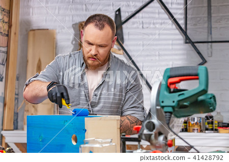 profession, carpentry, woodwork and people concept - carpenter working with wood plank and covers it 41428792