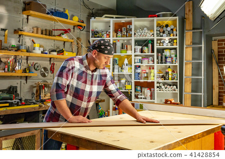 Carpenter doing his job in carpentry workshop. a man in a carpentry workshop measures and cuts Carpenter doing his job in carpentry workshop. a man in a carpentry workshop measures and cuts 41428854