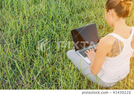 Back of young woman using laptop at meadows. 41430228