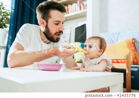 Good looking young man eating breakfast and feeding her baby girl at home 41435776