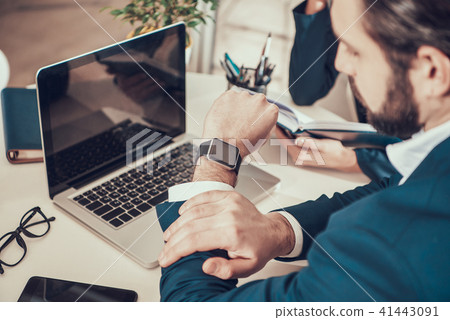 Worker looking at watch at desk in office. 41443091