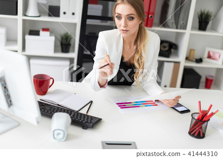 A young girl is sitting at the computer desk in the office, holding a pencil in her hand and working A young girl is sitting at the computer desk in the office, holding a pencil in her hand and working 41444310