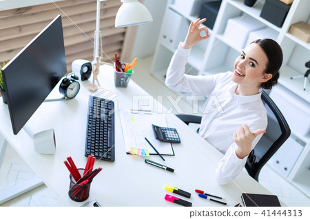 A young girl in the office sits at a table, works with documents and shows a sign of okay and class. 41444313