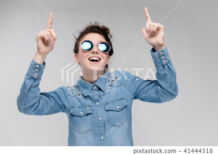 Young brunette girl in round glasses. Hairs are gathered in a bun. The girl points with her fingers. 41444318