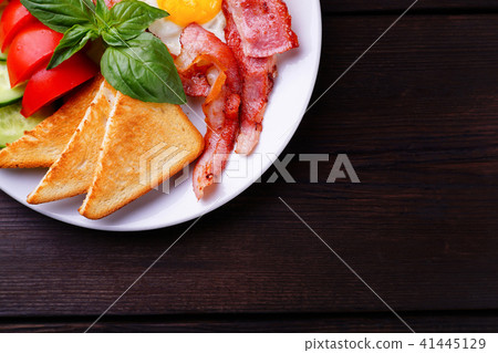 Fried eggs with bacon, toasts and fresh vegetables 41445129