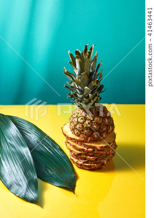 Composition of green leaves and sliced pineapple on a blue-yellow paper background Composition of green leaves and sliced pineapple on a blue-yellow paper background 41463441