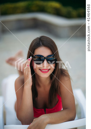Beautiful lady in sunglasses lies on a longer in front of the pool 41464568